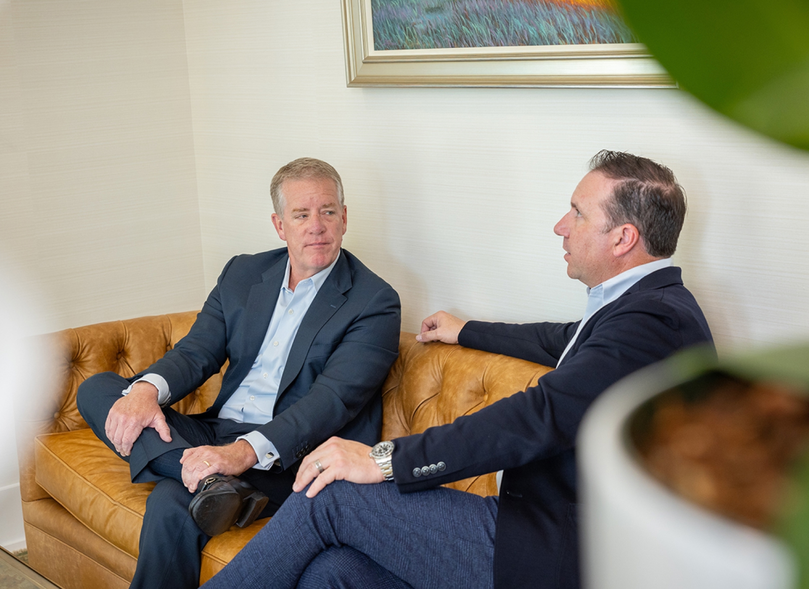 Two professionals in business attire seated on a leather couch, engaged in a thoughtful conversation, reflecting collaboration, trust, and personalized financial guidance.